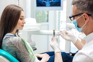 A dentist holds up a model of a dental implant while explaining to a female patient how it works