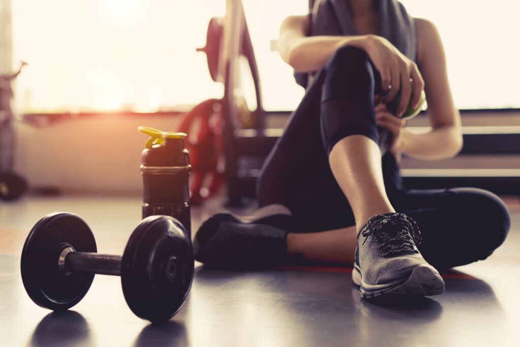 Woman sitting on floor at gym next to weights and water bottle